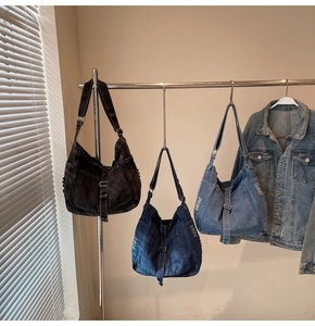 Three denim hobo bags in black and blue with frayed edges on a metal rack display