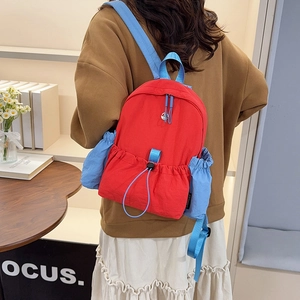 Seitenansicht des rot-blauen Rucksacks mit großer Vordertasche und Flaschenhalterung