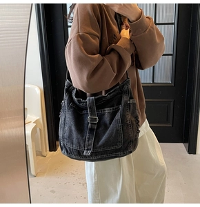 Close-up of black washed denim tote bag with white contrast stitching and metal buckle details