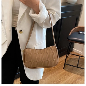 Detail of khaki quilted baguette bag with wave pattern and gold zipper on model