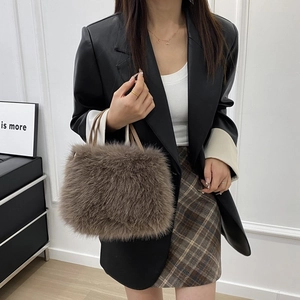 Elegante borsa a mano in peluche marrone con texture soffice e catena di perle su modella