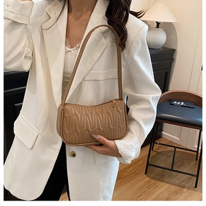 Model wearing a tan pleated baguette underarm bag with vertical wavy texture