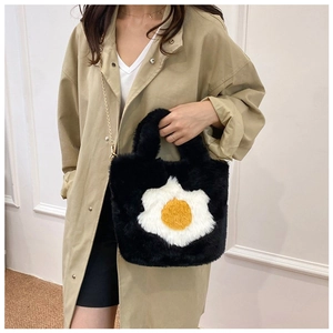 Chic black plush tote with fried egg motif and gold chain strap worn by a model