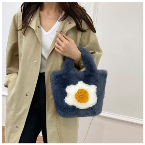 Detail of blue plush handbag with fried egg pattern and gold chain strap on model