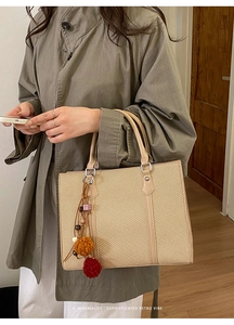 Detail der beige gewebten Tragetasche mit bunten Pompons und eleganten Ledergriffen