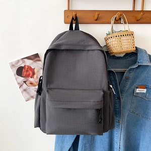 Detail of dark grey backpack with grid texture hanging on a wall with denim jacket
