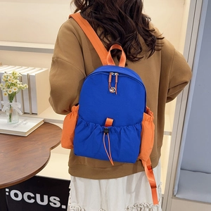 Blau-oranger Nylon-Rucksack an einem Model in einem gemütlichen Indoor-Lifestyle-Ambiente