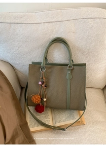 Detail einer salbeigrünen gewebten Handtasche mit Boho-Quasten-Anhänger auf Vintage-Büchern