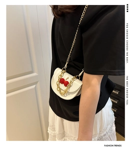 Gros plan du mini sac selle blanc avec cerises rouges et chaîne dorée élégante