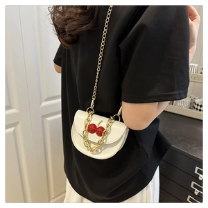 Gros plan d'un mini sac selle blanc avec cerise et chaîne dorée porté par un mannequin
