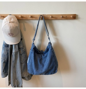 Detail of washed denim tote with frayed edges, adjustable strap and snap button