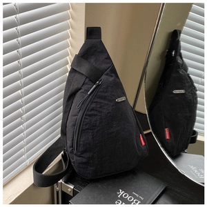 Close-up of black nylon crossbody bag featuring silver metal plate and red fashion label