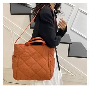 Detail showing the bright orange quilted tote bag texture and side pocket on a model