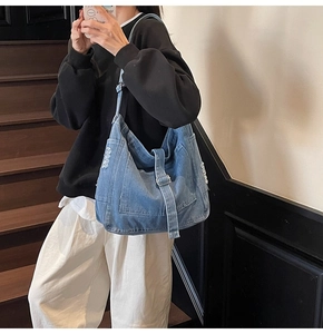 Detail of blue denim shoulder bag with frayed edges and metal buckle on wooden stairs
