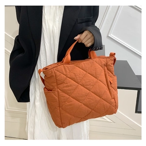 Detail of orange quilted puffer tote bag with adjustable strap and side pocket