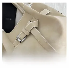 Close-up of beige faux leather handbag featuring silver buckle and white stitching details