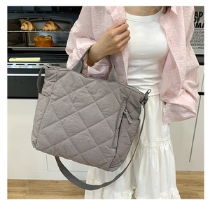 Detail of grey quilted puffer tote bag with front zipper pocket and adjustable strap