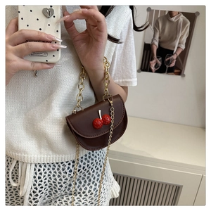 Détail d'un sac selle marron avec cerises et chaîne dorée sur un haut en maille blanc