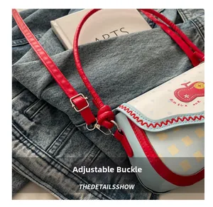 Detail of red leather shoulder strap with adjustable silver metal buckle on plaid bag