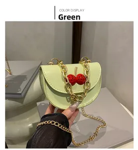 Gros plan sur un mini sac selle vert avec strass cerise et chaîne dorée de luxe
