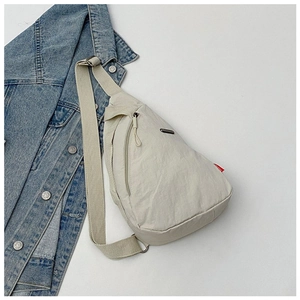 Detailed view of beige nylon crossbody chest bag on denim jacket backdrop