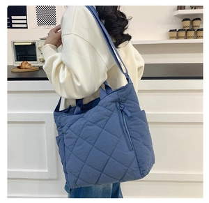 Blue quilted puffer tote bag with side zipper and dual straps in a lifestyle setting