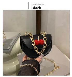 Détail d'un sac besace noir en cuir avec cerises en cristal et chaîne dorée