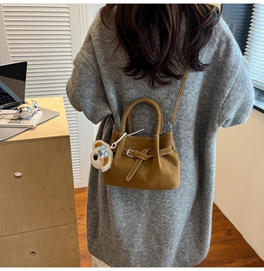 Close-up of caramel leather crossbody bag with belt detail and plush charm in lifestyle setting