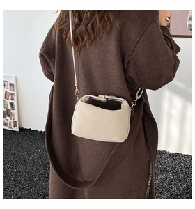 Sac bandoulière beige chic avec sangle réglable porté par un mannequin en manteau