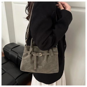 Detail of olive green suede tote bag showing fashion tag, gold buckle, and adjustable strap
