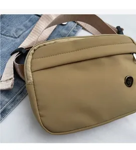 Detail showing the khaki nylon material, metal logo badge, and beige fabric shoulder strap