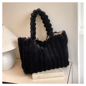 Detail of plush black tote bag featuring unique spherical pom-pom handle and vertical texture
