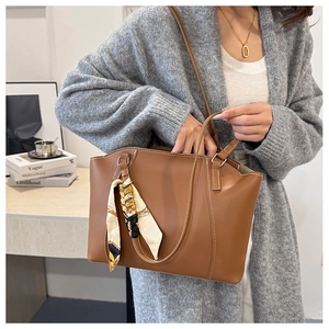 Detail of brown leather tote bag with white stitching and decorative handle scarf
