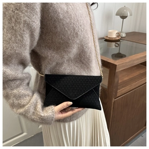 Elegant woman wearing black textured envelope crossbody bag with a golden chain strap