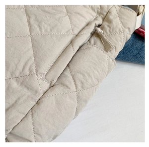 Detailed macro view of beige quilted tote bag showing rhombus stitching and zip closure