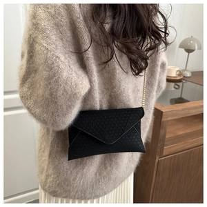Detail of black woven envelope crossbody bag with gold chain strap on model