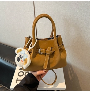 Detail of brown faux leather shoulder bag with buckle strap and plush dog charm