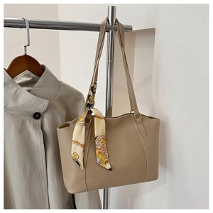 Detail of large beige tote bag with decorative silk scarf hanging on a metal rack