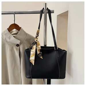 Detail of a black leather tote bag with contrast stitching and decorative silk scarf