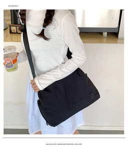Close-up of black nylon shoulder bag with adjustable strap and logo detail on model