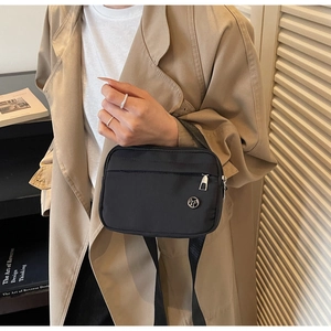 Detail of minimalist black nylon crossbody bag with silver logo shown in lifestyle setting