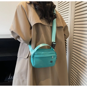 Close-up of mint green nylon crossbody bag showing the zipper pocket and strap detail