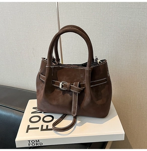 Close-up of brown suede small square bag with decorative buckle and white contrast stitching