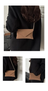 Detail view of brown envelope crossbody bag featuring woven texture and gold chain strap
