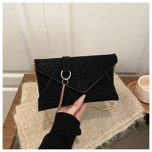 Close-up of black envelope clutch with woven texture and gold snake chain strap