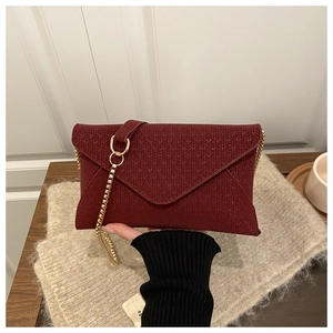 Detail of burgundy envelope clutch featuring woven texture and a gold chain strap