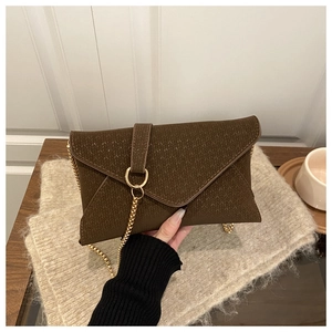 Detail of dark brown knitted envelope bag with gold chain strap on a warm textured background