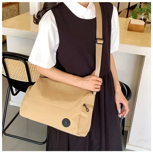 Detail of khaki nylon crossbody bag featuring wide adjustable strap and brand patch