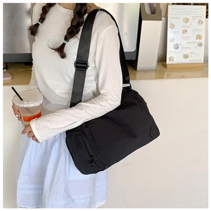 Detail of a large black nylon bucket bag with a wide adjustable strap and zipper pocket
