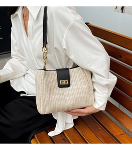 Close-up of woven straw tote bag with black leather flap and golden chain strap